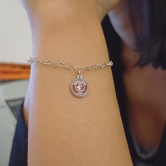 Questo braccialetto in argento 925 ha una catena di maglie a forma di cuore e una medaglietta rotonda da 10 mm. La superficie della medaglietta è lavorata artigianalmente nel nostro laboratorio orafo a Livorno e presenta il logo della Libertas Livorno 1947, inciso a laser e smaltato a caldo con un ricco colore amaranto. È un pezzo elegante e sportivo, pensato per celebrare la passione e l'appartenenza. Ideale per chi cerca gioielli personalizzati e distintivi.